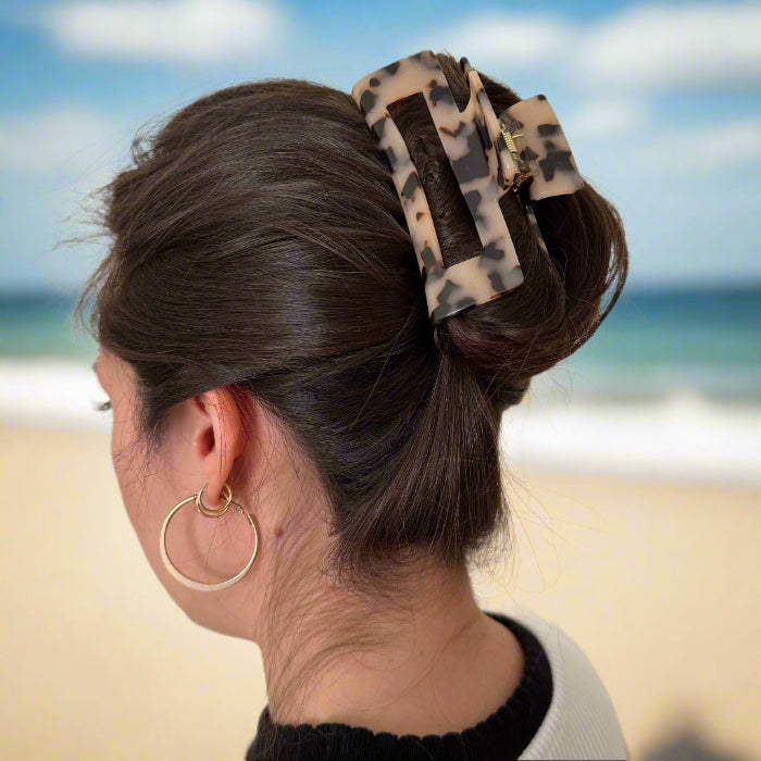 Model with long brown hair wearing a blonde tortoiseshell rectangular hair claw clip made from cellulose acetate, shown from behind