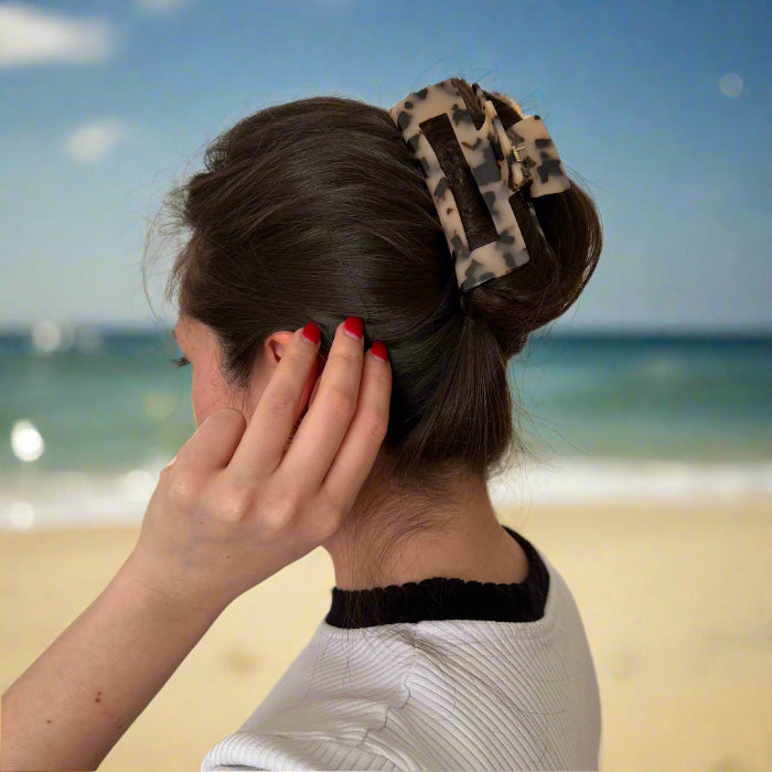 Model gently touching her hair while wearing a blonde tortoiseshell rectangular hair claw clip, shown from behind