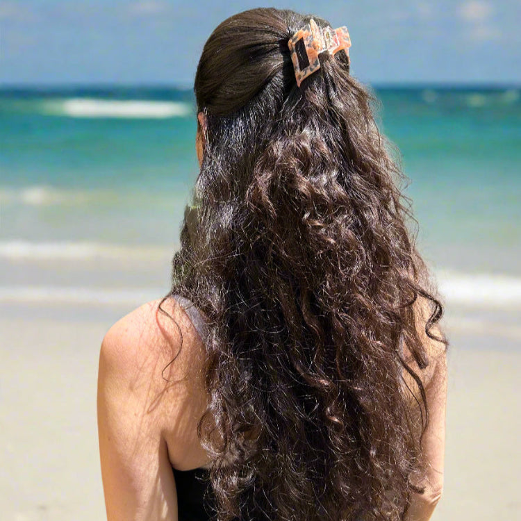 Woman with long hair styled in a half-up look wearing the Peach Gloss hair claw clip, standing at the beach in natural light.