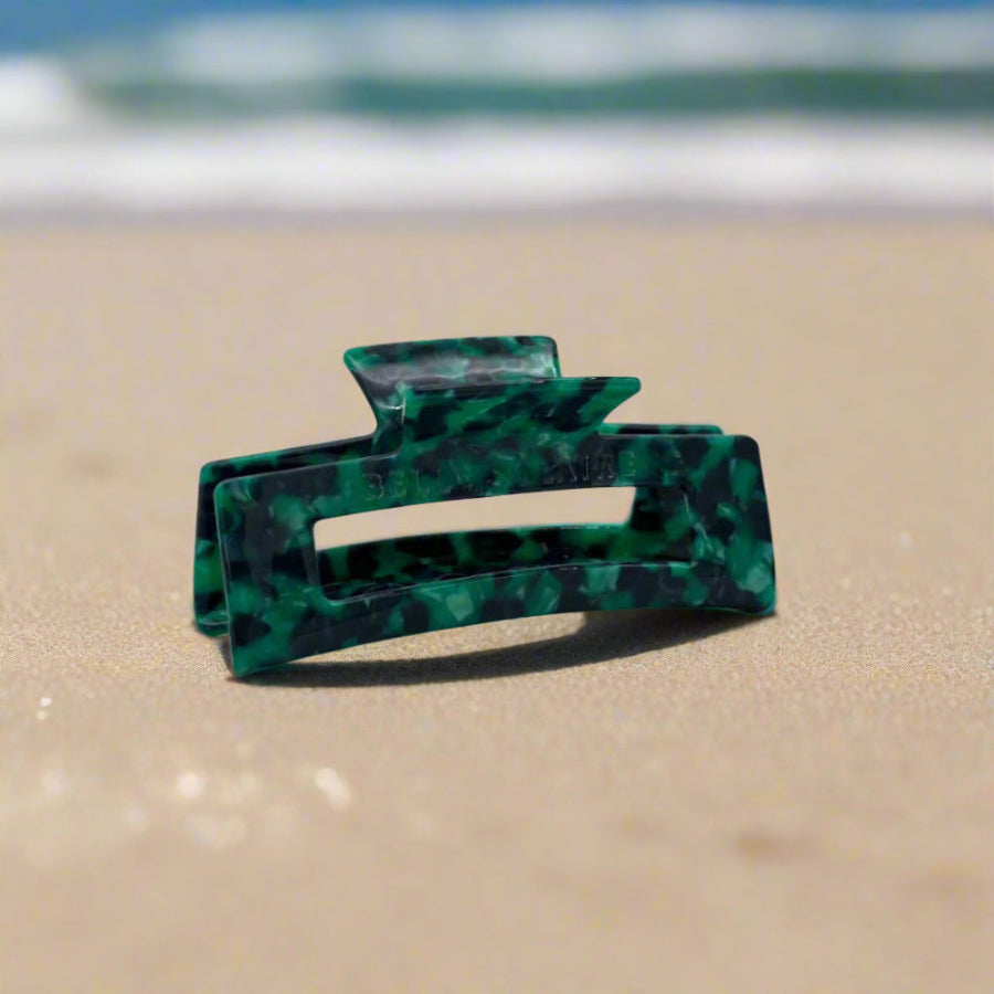 Emerald Grove hair claw clip featuring deep emerald green with touches of dark teal and smoky black, laid on a beach background.