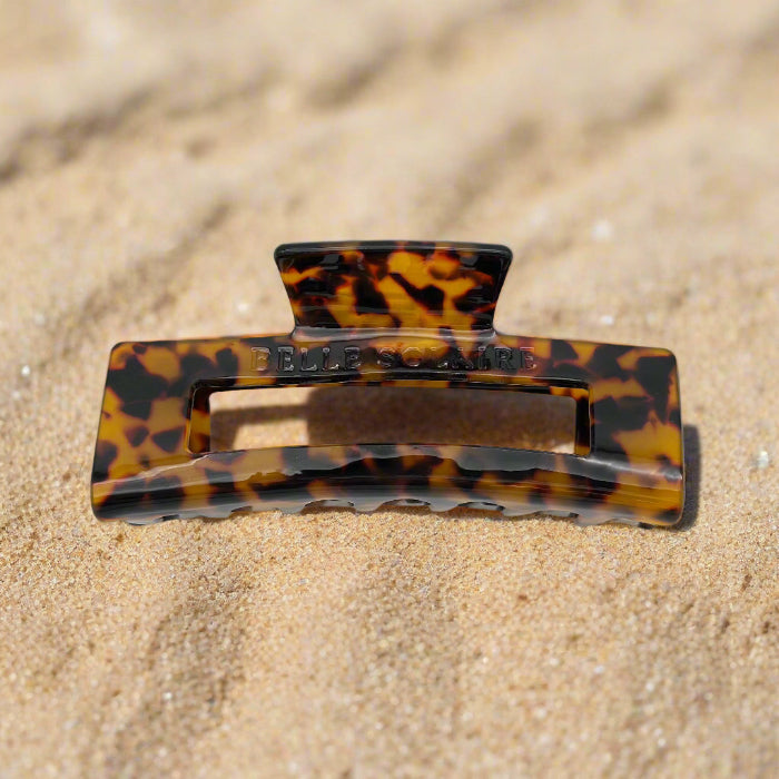 Dark tortoiseshell rectangular hair claw clip made from plant-based cellulose acetate, front view on beach.