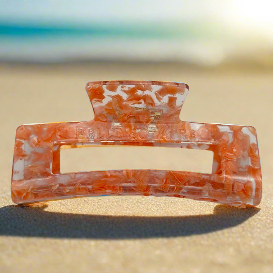 Front view of Peach Gloss rectangular hair claw clip in glossy peach tones, made from cellulose acetate, placed on beach sand.