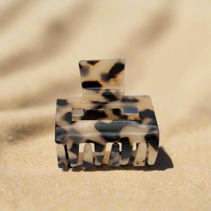 Small blonde tortoiseshell hair claw clip tilted to reveal interlocking claws, made from plant-based cellulose acetate, on beach
