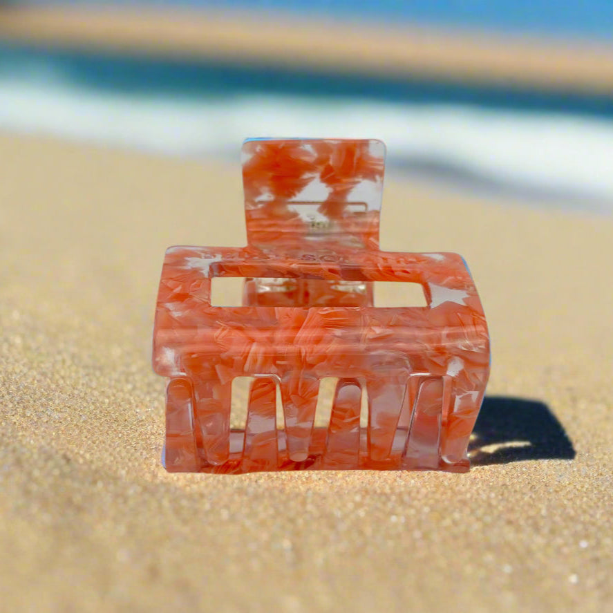 Peach Gloss hair claw clip displayed to show inner claws and hinge detail, made from eco-friendly cellulose acetate, on sand background.