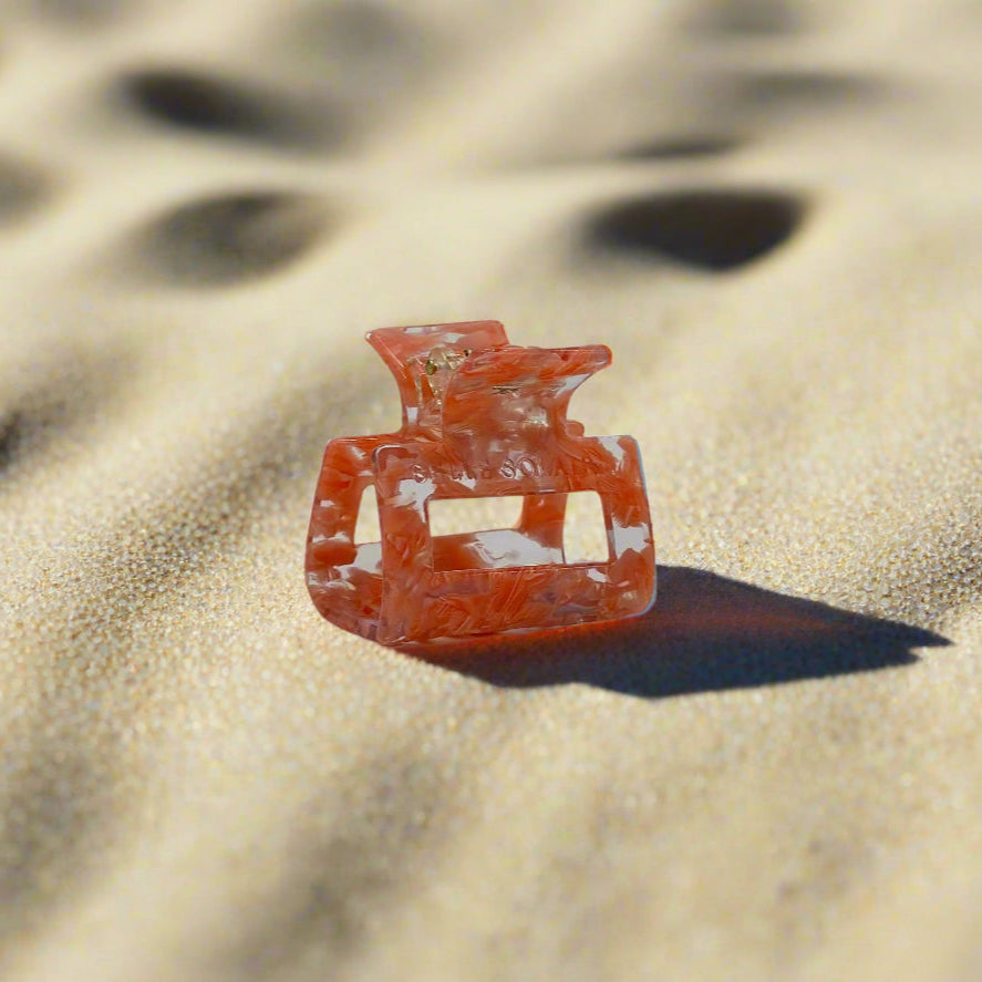 Peach Gloss hair claw clip made from plant-based cellulose acetate, shown in a slightly angled view on beach sand background.