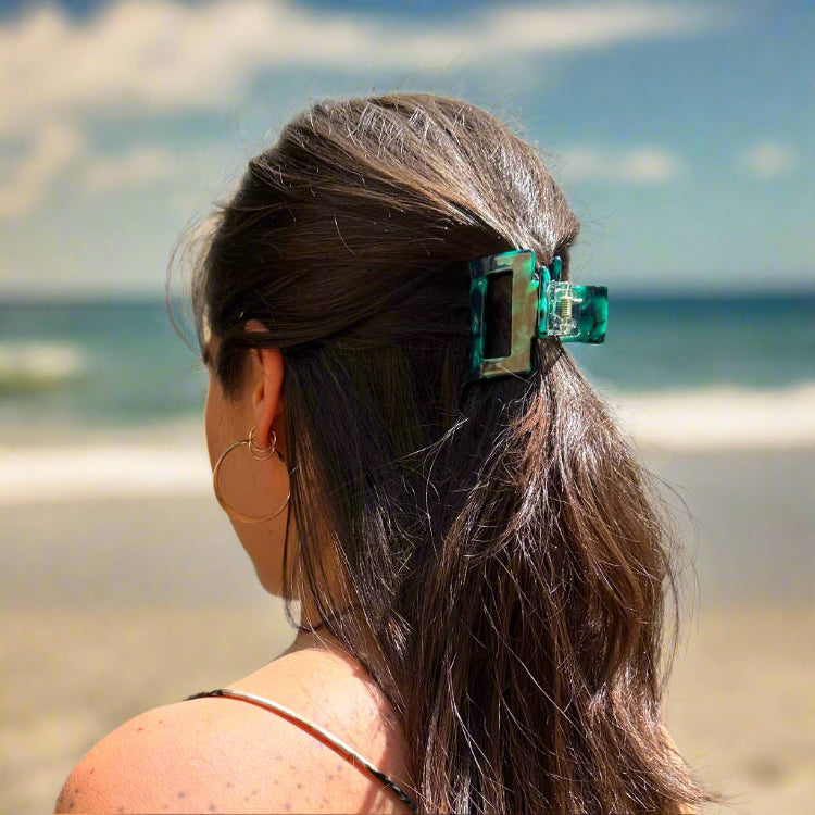 Model wearing the Emerald Grove clip at the beach, styled in long hair. Clip featuring dark green and teal hues.
