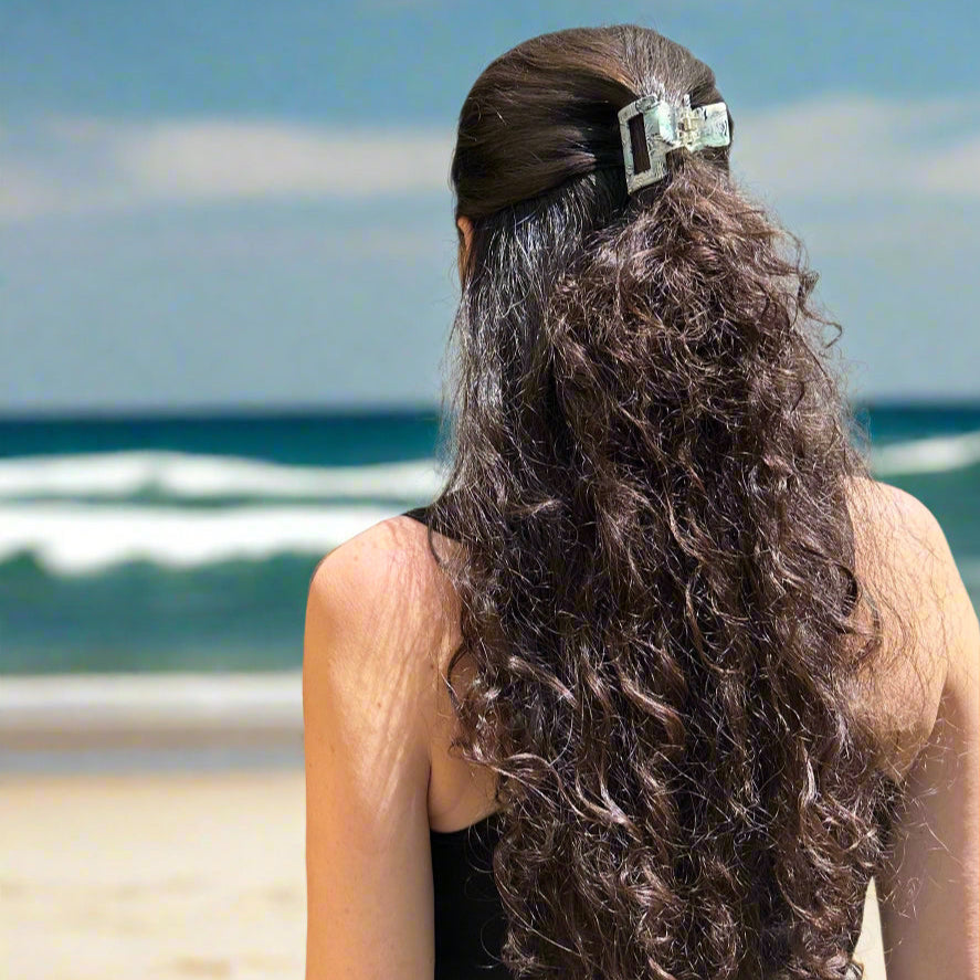 Woman wearing the Zebra Haze hair claw clip, styled in half up long hair, standing at the beach.