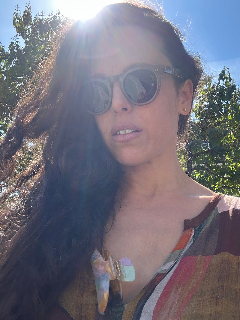 Woman wearing sunglasses with the sun rays shining behind her.