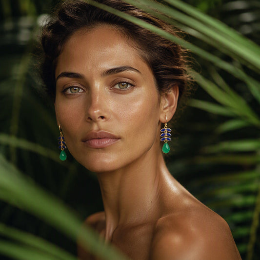 A close-up portrait of a woman with green teardrop earrings, framed by lush green palm leaves against a dark background.