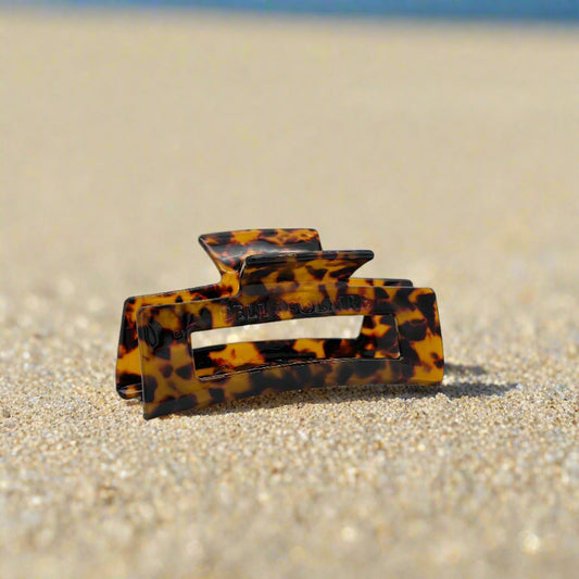 Dark tortoiseshell rectangular hair claw clip made from plant-based cellulose acetate, displayed on beach
