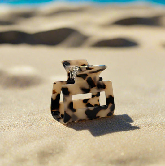 Small blonde tortoiseshell rectangular hair claw clip made from plant-based cellulose acetate, displayed on beach