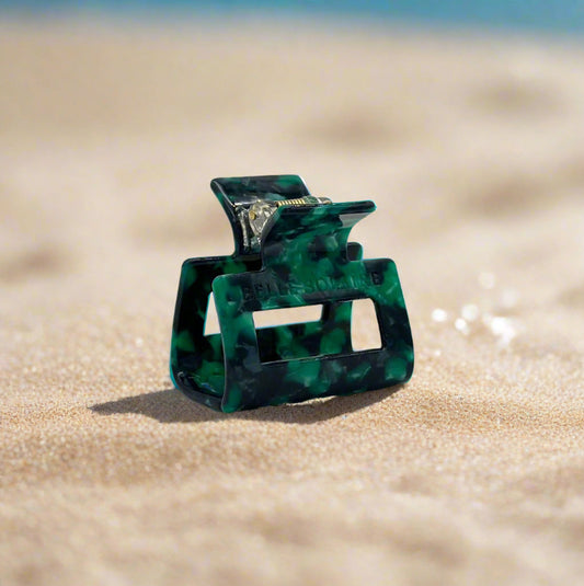 Emerald Grove hair claw clip featuring deep emerald green with touches of dark teal and smoky black, laid on a beach background.