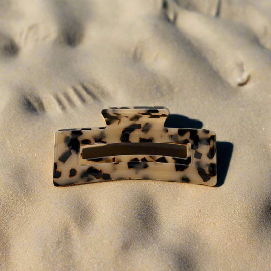 Blonde tortoiseshell rectangular hair claw clip made from plant-based cellulose acetate, front view on beach