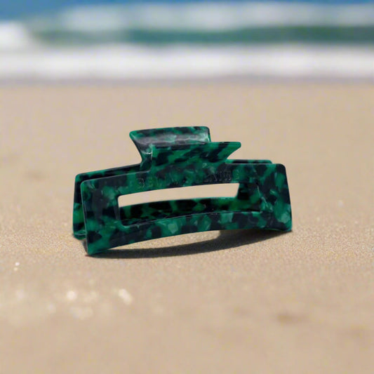 Emerald Grove hair claw clip featuring deep emerald green with touches of dark teal and smoky black, laid on a beach background.