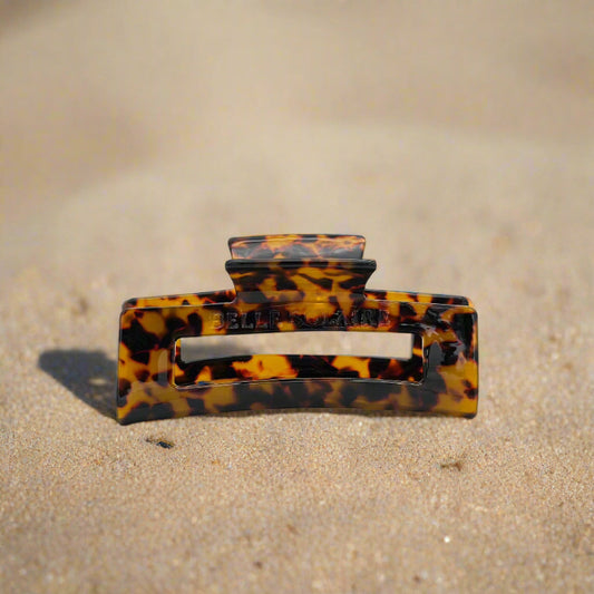 Dark tortoiseshell rectangular hair claw clip made from plant-based cellulose acetate, front view on beach.