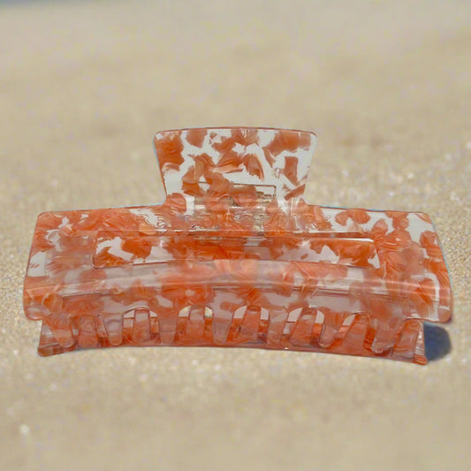 Peach Gloss hair claw clip displayed to show inner claws and hinge detail, made from eco-friendly cellulose acetate, on sand background.