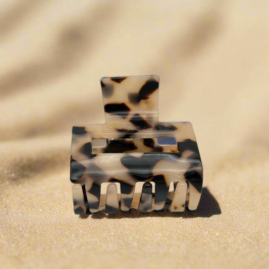 Small blonde tortoiseshell hair claw clip tilted to reveal interlocking claws, made from plant-based cellulose acetate, on beach
