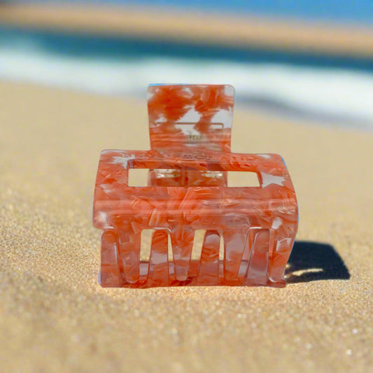 Peach Gloss hair claw clip displayed to show inner claws and hinge detail, made from eco-friendly cellulose acetate, on sand background.