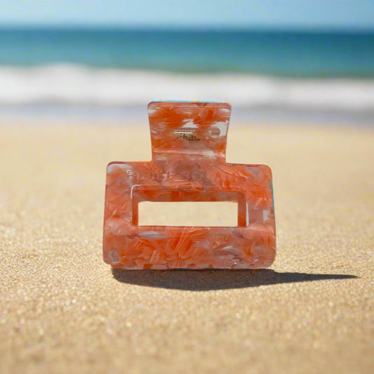 Front view of Peach Gloss rectangular hair claw clip in glossy peach tones, made from cellulose acetate, placed on beach sand.