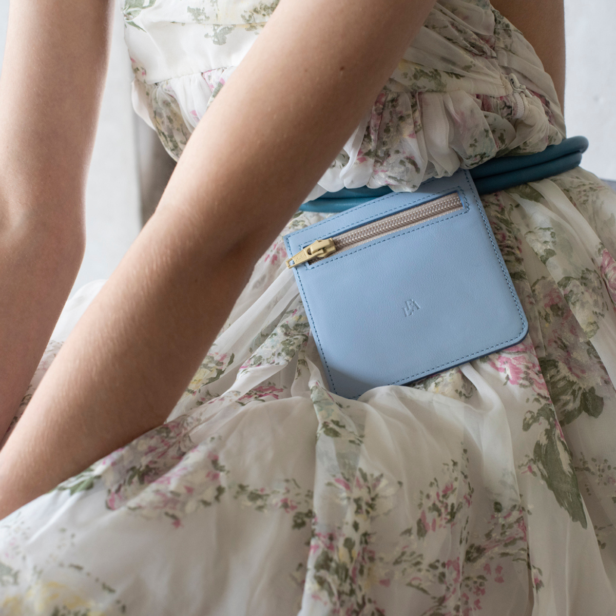 Light blue leather wallet with gold zipper on a floral dress