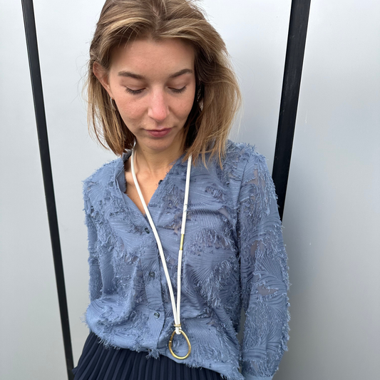 Woman wearing a blue lace blouse with a white leather multipurpose / lanyard around her neck.