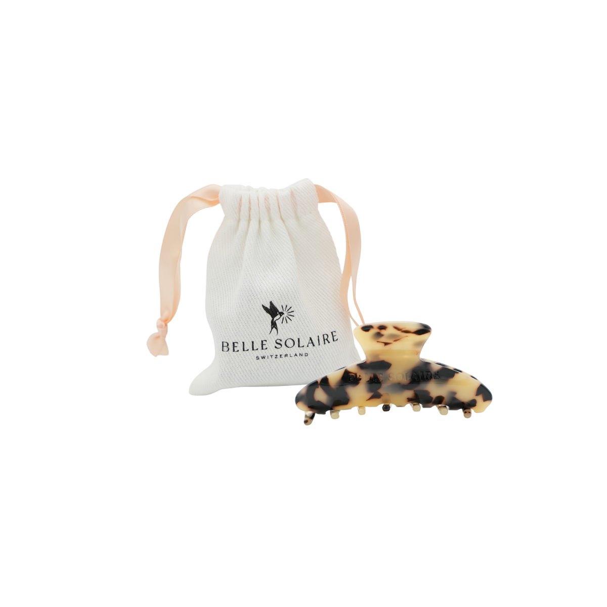 A blonde tortoise hair claw clip displayed next to its white drawstring pouch, which features the black printed logo 'BELLE SOLAIRE SWITZERLAND'.